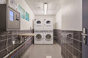 Un cuarto de lavandería con cuatro lavadoras, un panel de control y piso de baldosas.