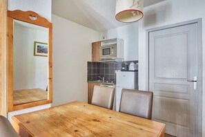 Cocina compacta con microondas, cafetera y refrigerador. Cuenta con una mesa de comedor de madera y sillas.
