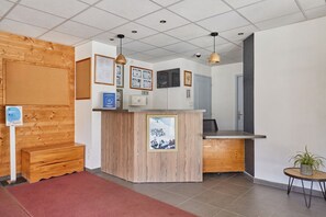 A reception area with a wooden counter, framed pictures, a small table with a plant, and a red carpet.