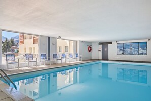 A swimming pool with clear blue water, surrounded by lounge chairs and a view of mountains.
