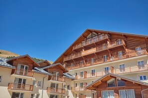 Un chalet de madera de varios pisos con balcones, un telesilla de esquí al fondo y un cielo azul despejado.