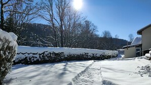 Een besneeuwde pad naar een gebouw, met een bordje dat een spa en sauna aangeeft, omringd door sneeuwzware bomen en een heldere lucht.