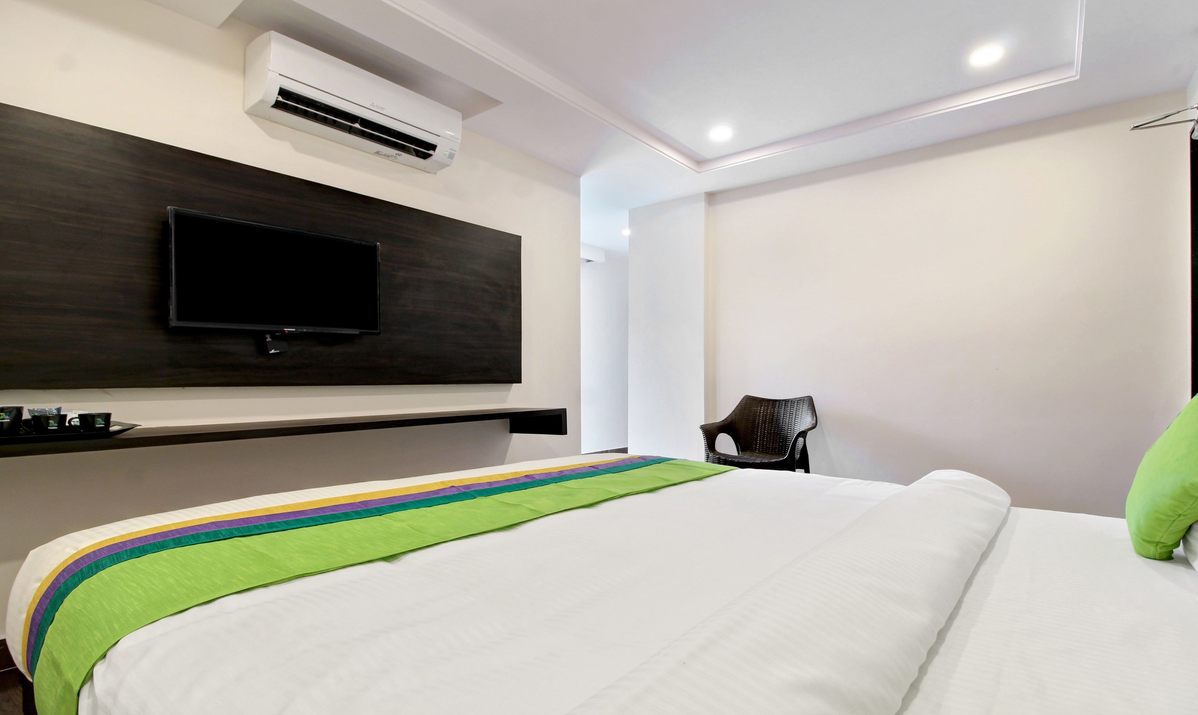 A hotel room with a bed, a flat-screen TV mounted on the wall, and a chair.