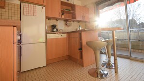 Une cuisine avec des meubles de rangement en bois, un réfrigérateur blanc, une machine à café et un tabouret de bar.