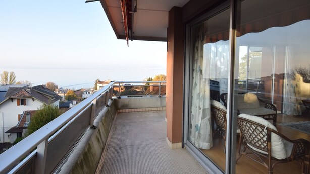 Un balcon avec vue sur la mer, une porte vitrée et un fauteuil en osier.