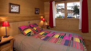 A cozy wooden room with a bed, two bedside lamps, and a window with curtains.