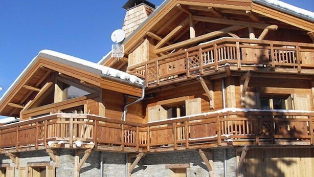 A wooden chalet with multiple balconies, stone foundation, and a chimney.