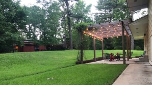 A well-maintained lawn with a wooden pergola adorned with string lights, a patio area with chairs, and a brick pathway leading to a house. - Quiet Home less than a mile from Vaught Hemingway (Oxford)