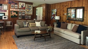 A cozy living room with wooden paneling, two sofas, a coffee table, and various framed pictures and posters on the walls. - Quiet Home less than a mile from Vaught Hemingway (Oxford)