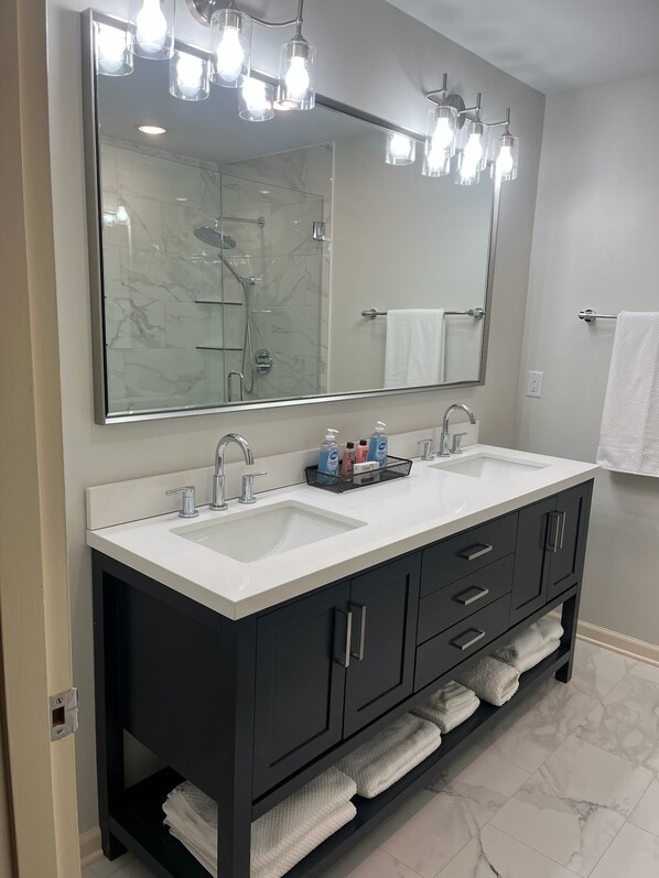 A modern bathroom with a double sink vanity, a large mirror, and a shower.