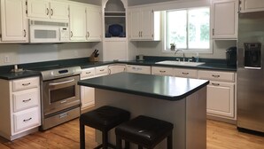 A modern kitchen with white cabinets, a stainless steel refrigerator, a microwave, and a sink. There is a window providing natural light and a small island with stools. - Quiet Home less than a mile from Vaught Hemingway (Oxford)