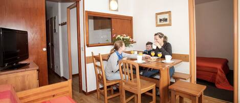 A cozy dining area with wooden furniture, a television, and a bed in the background.