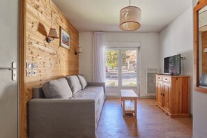 Quarto acolhedor com parede de madeira, sofá cinza, armário de madeira e uma televisão.