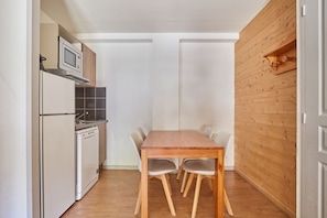 A compact kitchen with a refrigerator, microwave, and dishwasher, a wooden table with chairs, and a wooden wall.