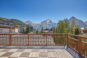 Um deck de madeira com guarda-corpo, com vista para uma paisagem montanhosa e edifícios ao fundo.