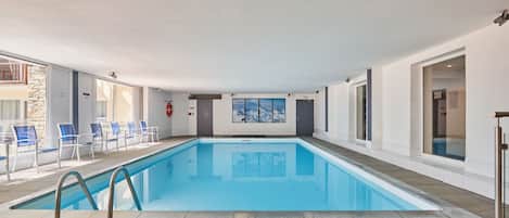 Una piscina interior con agua cristalina azul, rodeada de paredes blancas y suelo de baldosas.
