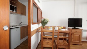 A compact kitchen with wooden cabinets, a microwave, a sink, and a dining area with a table and chairs. - Studio cosy 200m des remontées mécaniques! (Tignes)