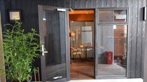 Un edificio moderno con un gran ventanal corredera que da a un espacio interior con una mesa y sillas para comer.