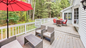 Une terrasse en bois avec des meubles en osier et un parasol rouge.