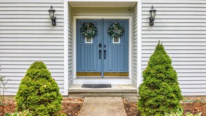 Une maison avec une porte d’entrée bleue, deux petits arbres à feuilles persistantes en pot et deux lanternes fixées au mur.