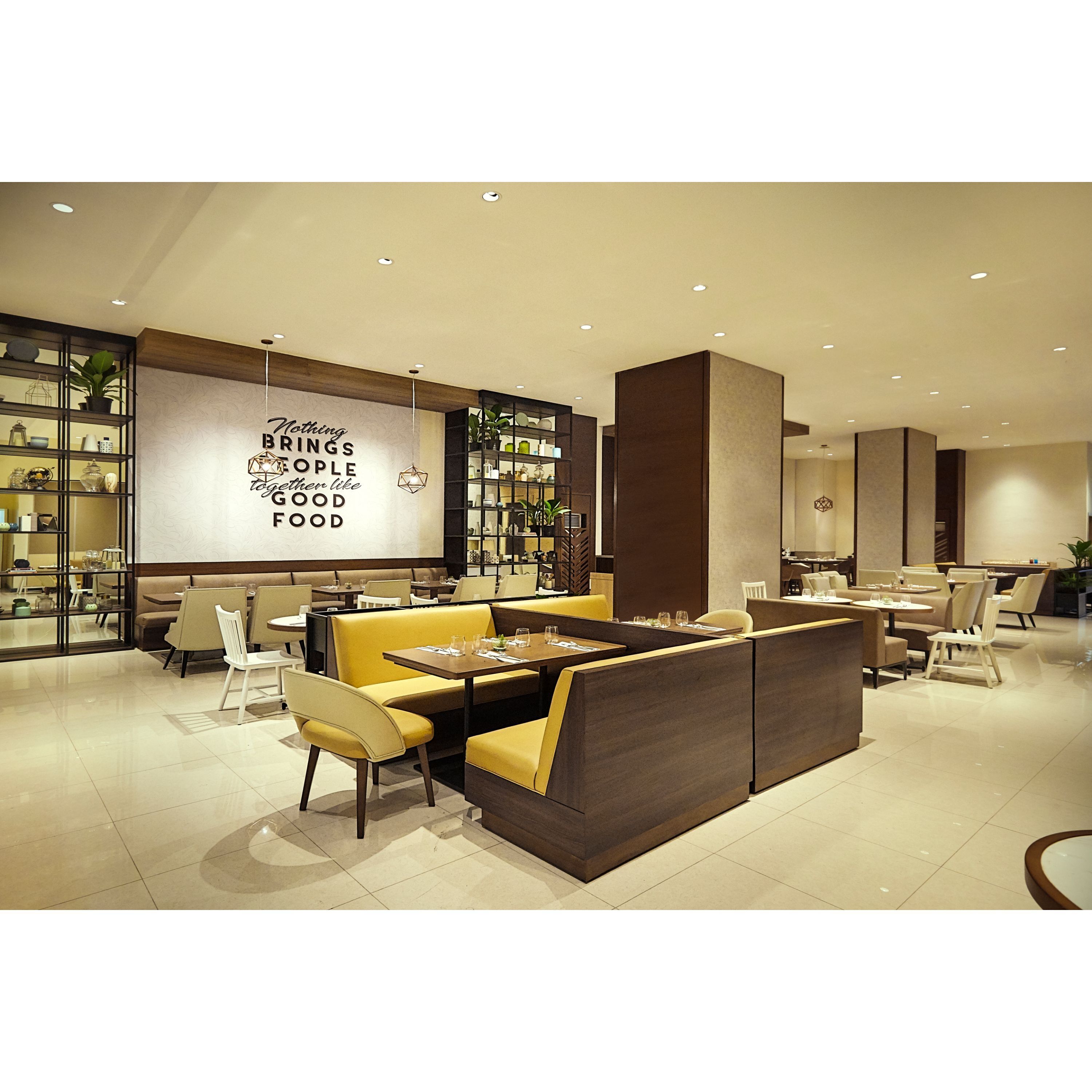 A modern restaurant interior with a central seating area, high ceilings, and a decorative wall with a quote.