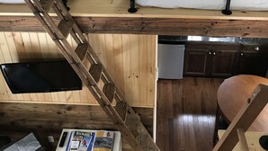 A loft bedroom with two beds, a ladder, a small table with books, and a window. - The in town cabin  (Conway)