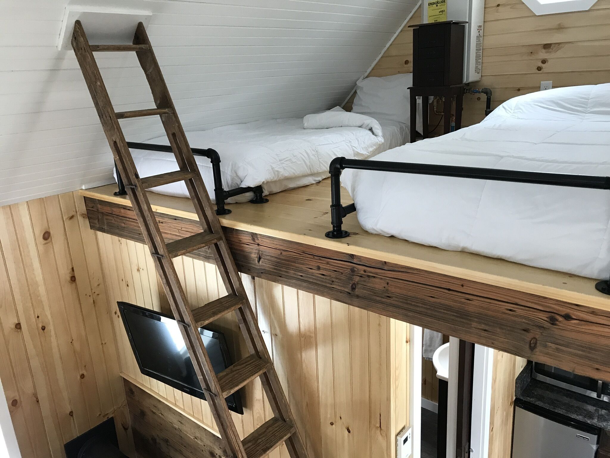 Une chambre de style « loft », avec un plancher en bois, une échelle, un lit, un bureau et un téléviseur.