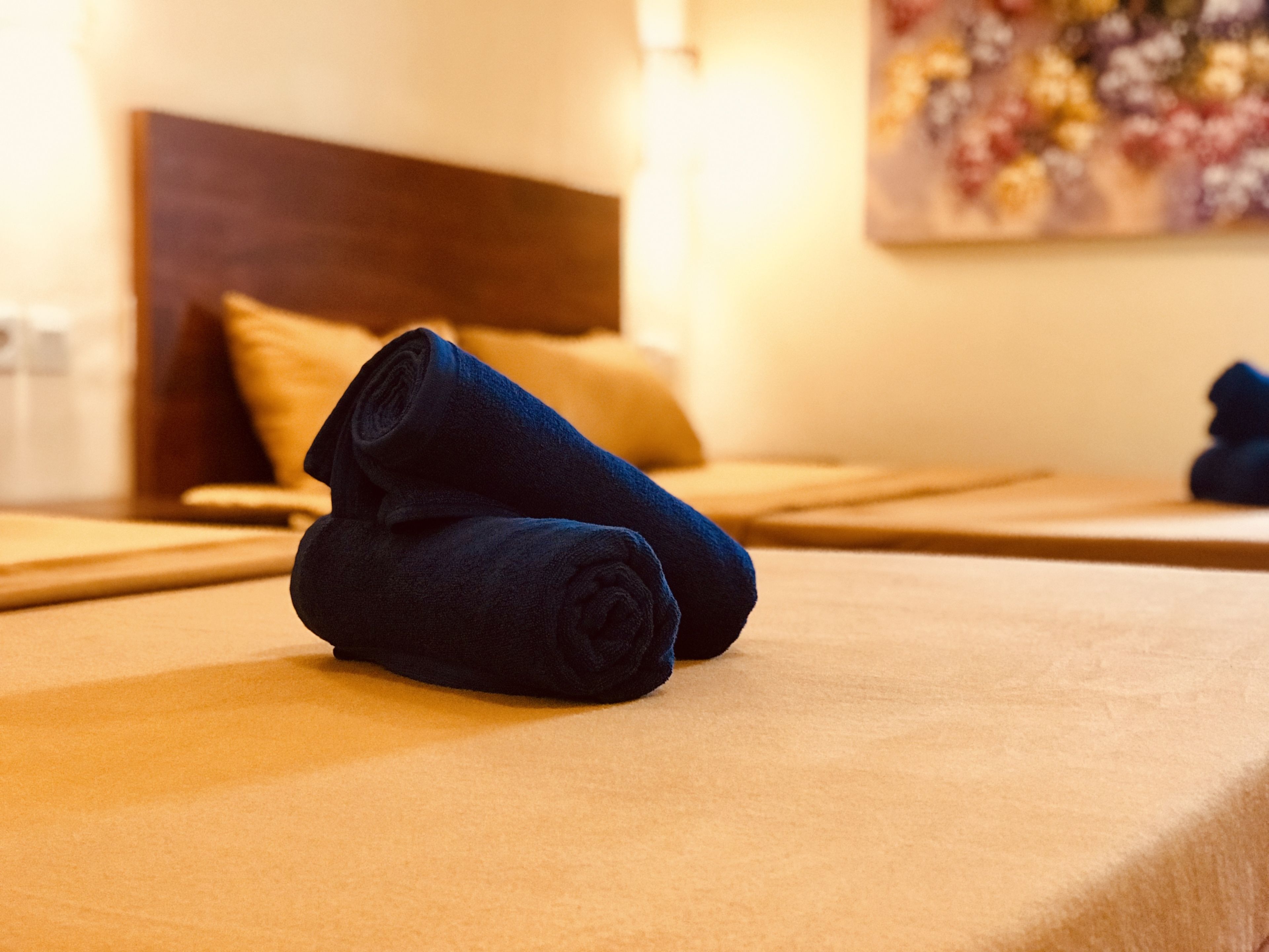A hotel room with a neatly made bed, a headboard, and a painting on the wall.