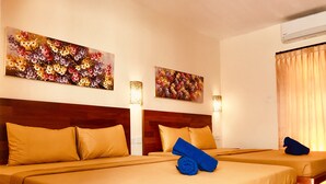 Ein Hotelzimmer mit zwei Betten, jeweils mit einem Holz-Kopfteil und beiger Bettwäsche. An den Wänden befinden sich Blumengemälde und auf einem Bett liegt ein blaues Handtuch.