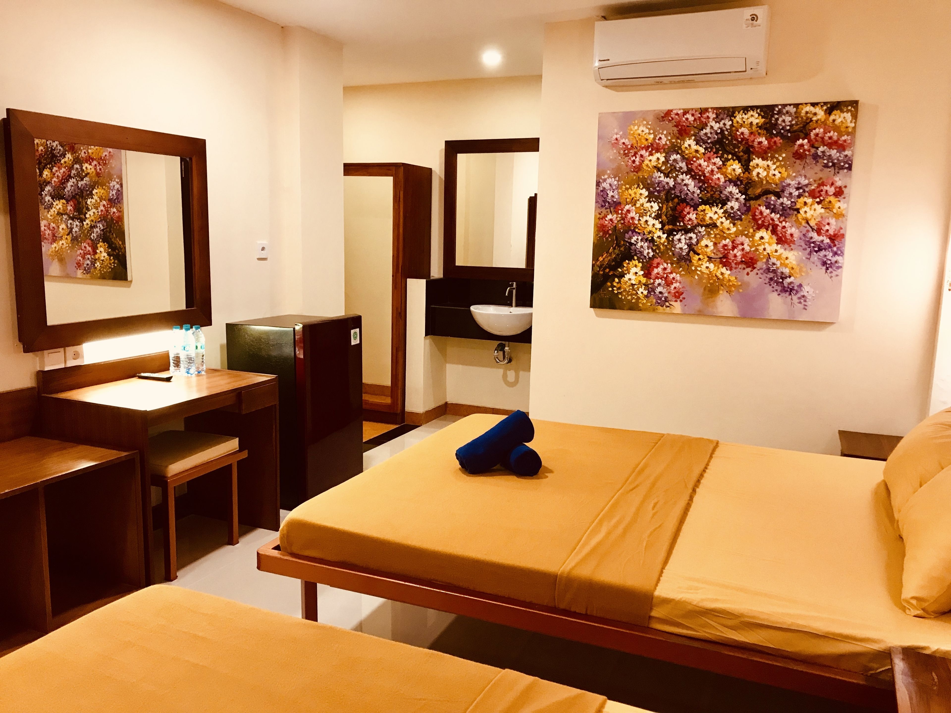 Ein Hotelzimmer mit einem Bett, einem Schreibtisch mit Stuhl, einem Spiegel, einem Waschbecken und einem Blumenbild.