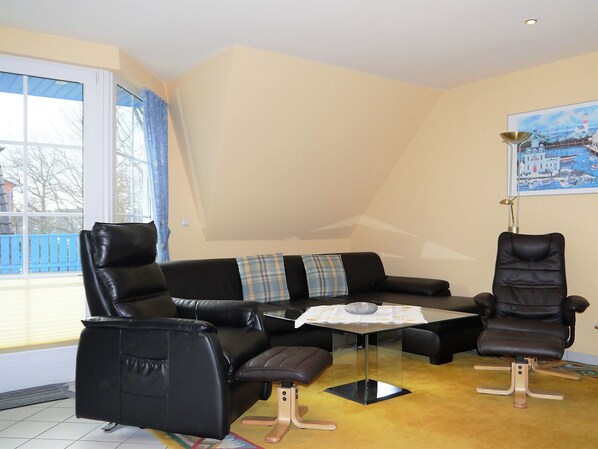Un salon moderne avec un canapé en cuir noir, un fauteuil assorti et une table basse en verre.