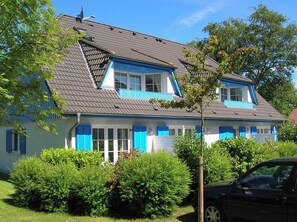 Une maison à deux étages avec un toit en pente, des volets bleus et un jardin à l’avant.