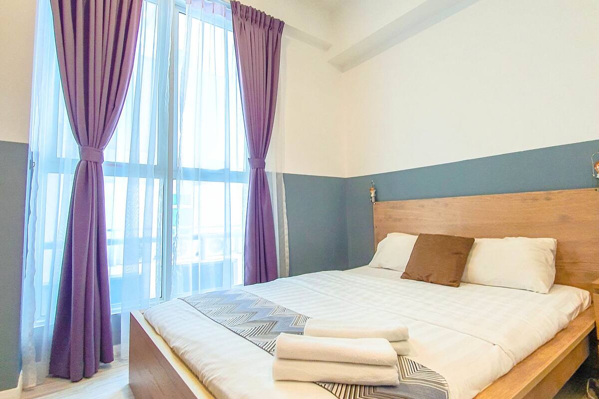 A modern bedroom with a large bed, wooden headboard, and purple curtains.