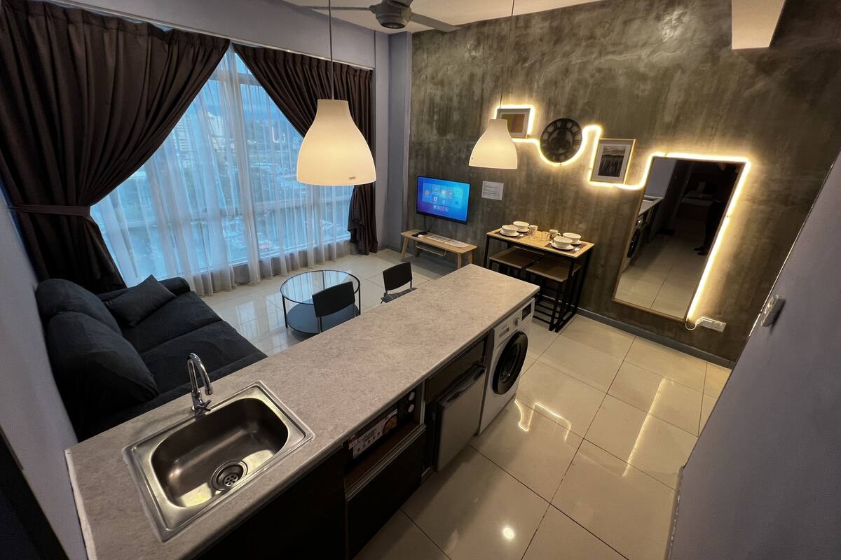 A modern kitchen with a sink, stove, and dining area. There is a large window with curtains, a ceiling fan, and a flat-screen TV.