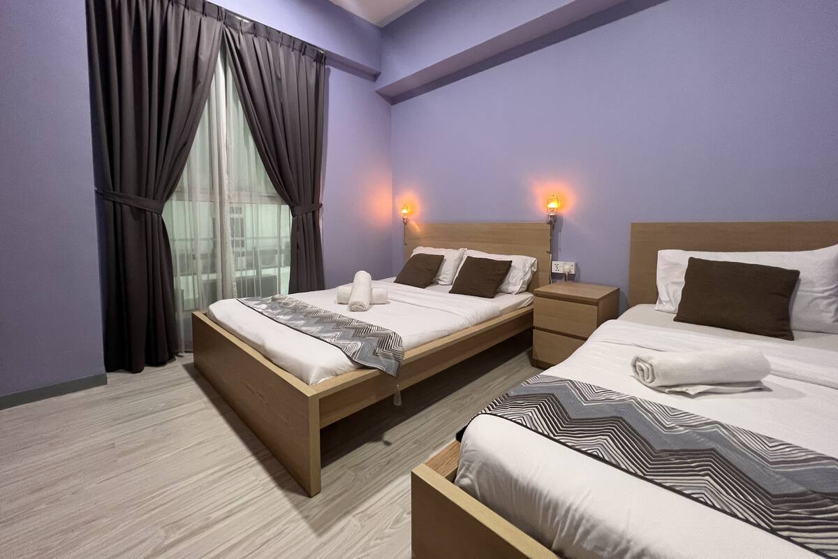 A hotel room with two beds, a nightstand, a window with curtains, and wall-mounted lights.