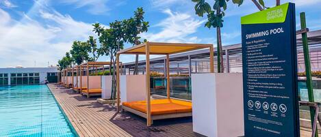 A swimming pool area with wooden deck, sun loungers, and a sign detailing pool rules and regulations.