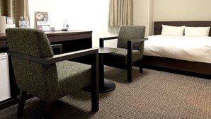 A hotel room with a bed, two armchairs, a small table, a desk, and a window with curtains. - HOTEL GLAN Y's KUMAGAYAEKIMAE premier (Kumagaya)