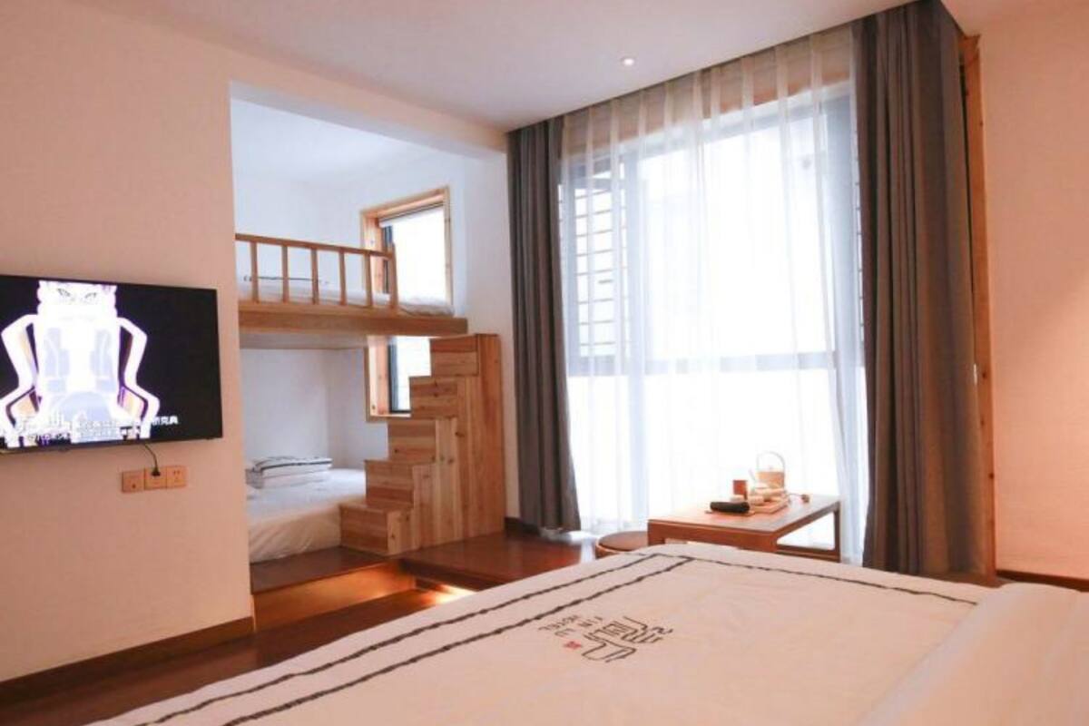 A hotel room with a large bed, a TV mounted on the wall, a wooden staircase, and a window with curtains.