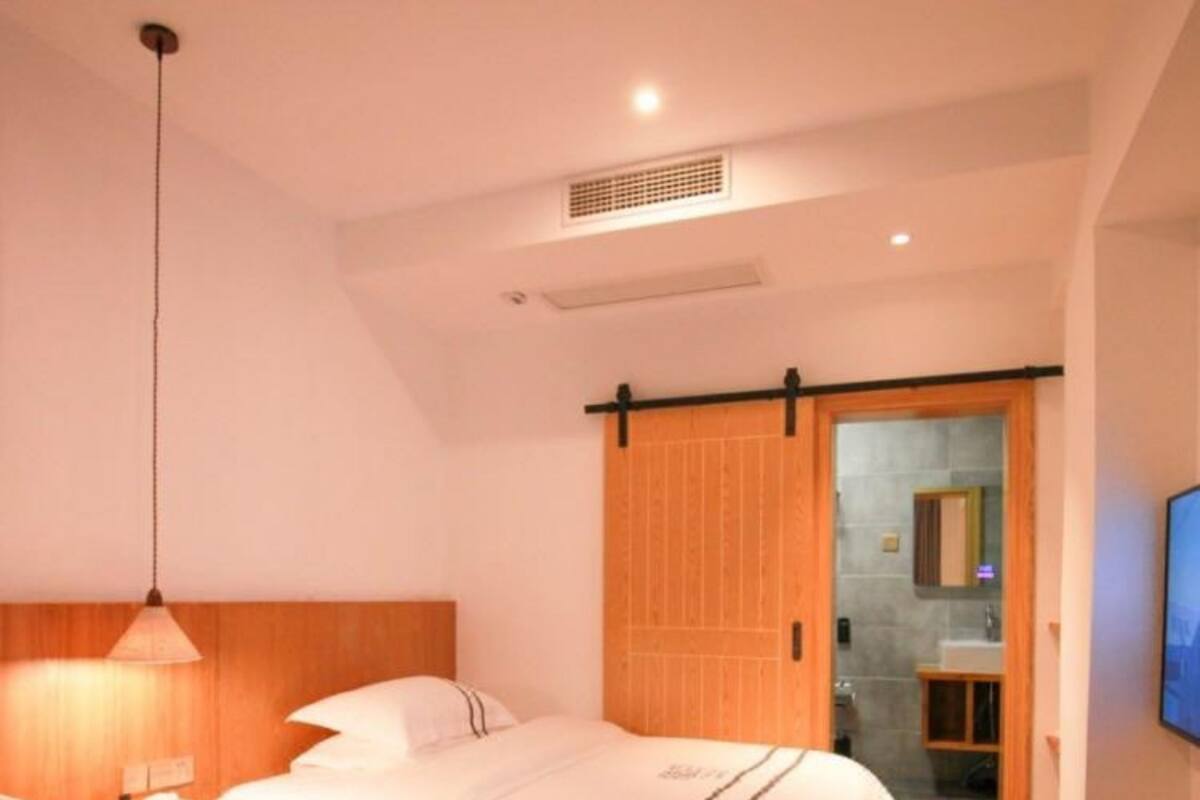 A hotel room with two beds, a wooden headboard, a sliding door to a bathroom, and a TV on the wall.