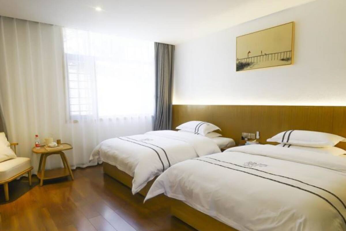 A hotel room with two beds, a wooden floor, a small table, and a painting on the wall.