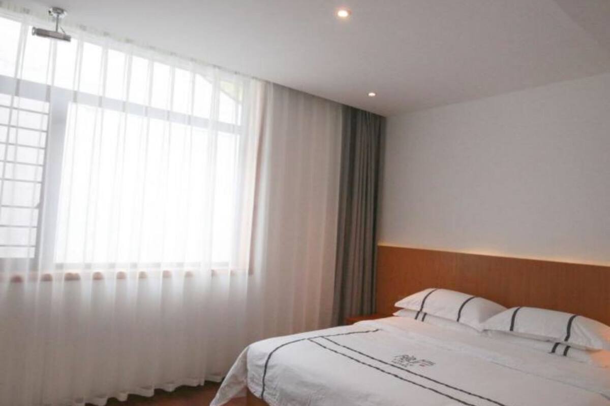A hotel room with a large bed, a window with sheer curtains, and a wooden headboard.