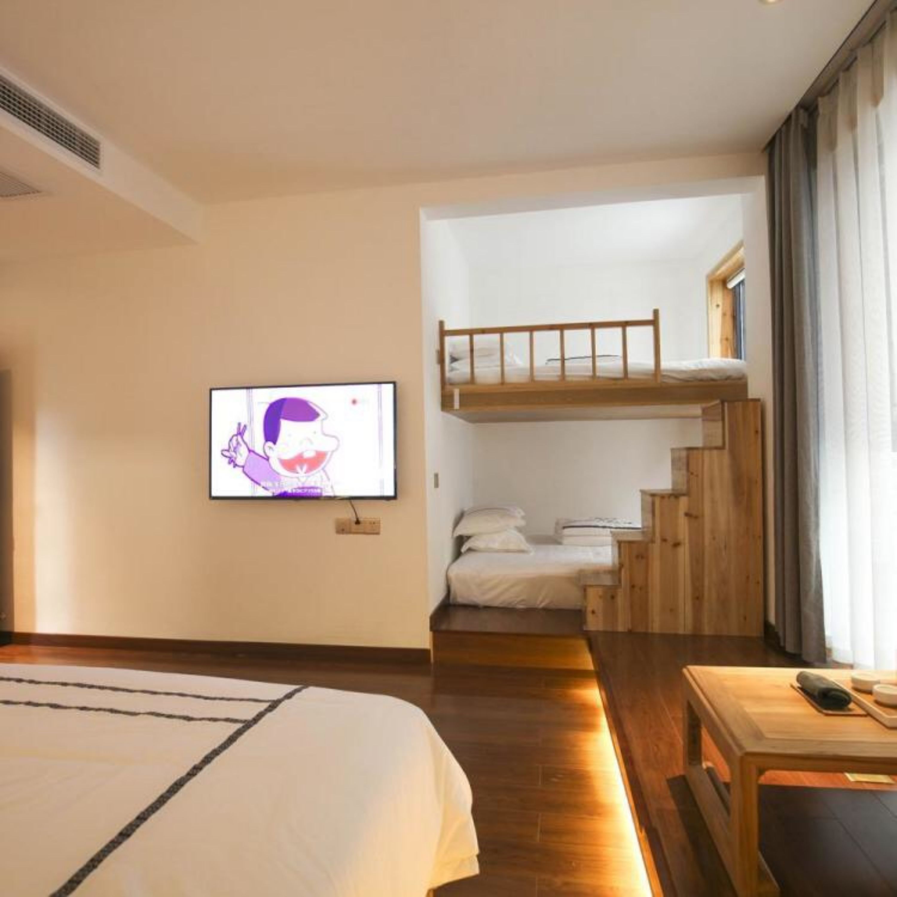 A hotel room with a bunk bed, a television, a desk, and a window with curtains.