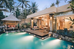 A modern resort with a swimming pool, outdoor seating, and a well-lit entrance.