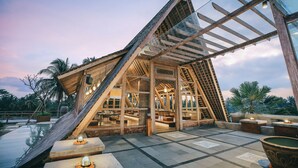A modern, open-plan interior with a sloped roof, large windows, and a pool area. - Kuwarasan A Pramana Experience (Tegallalang)