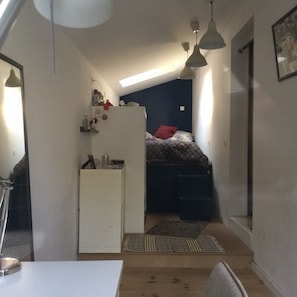 Ein kleines Zimmer mit Bett, einer Küchenzeile und einem Schreibtisch.