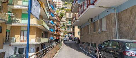 A narrow street with multi-story buildings, balconies, and parked cars.