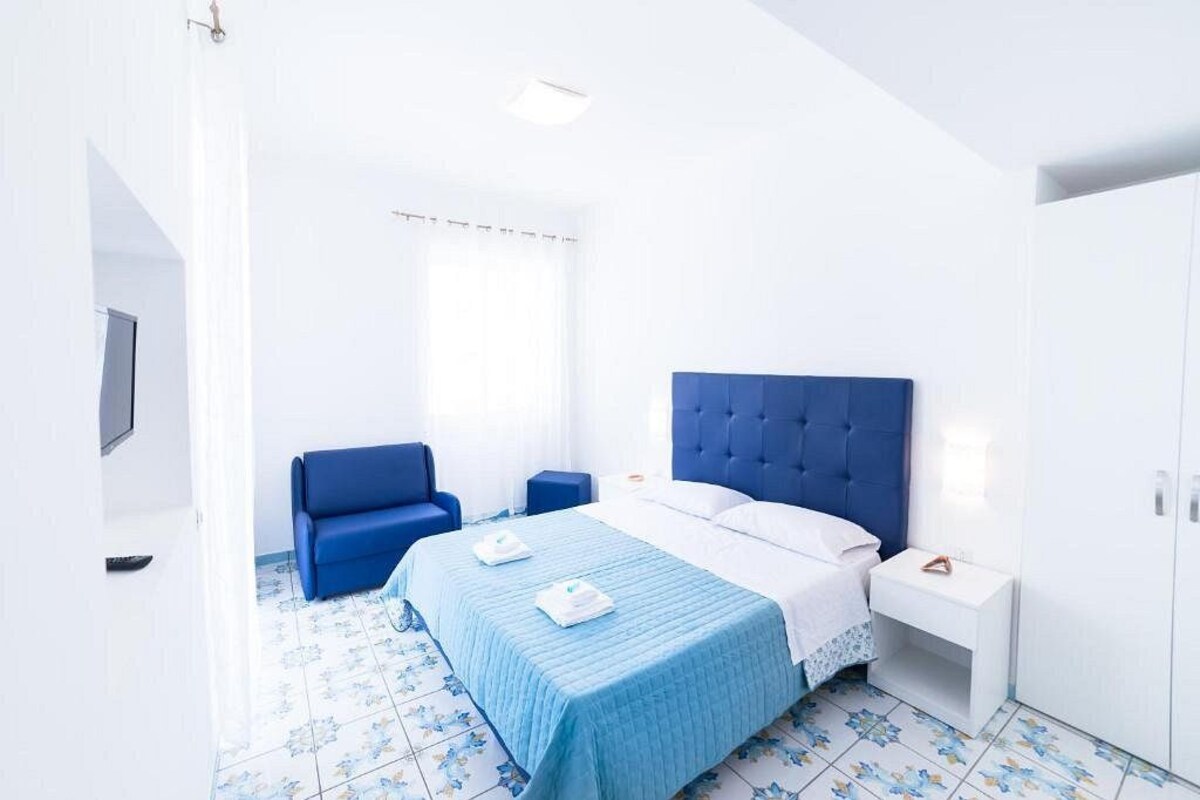 A hotel room with a bed, a blue sofa, a nightstand, and a wardrobe.