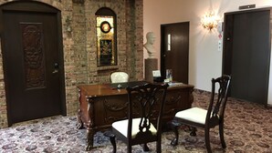 A room with a brick wall, a wooden desk, two chairs, a bust sculpture, and a stained glass window. - Deluxe Queen Room in Minneapolis Boutique Hotel (Minneapolis)