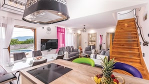 Un salon moderne comprenant un coin repas, un téléviseur et un escalier en bois.