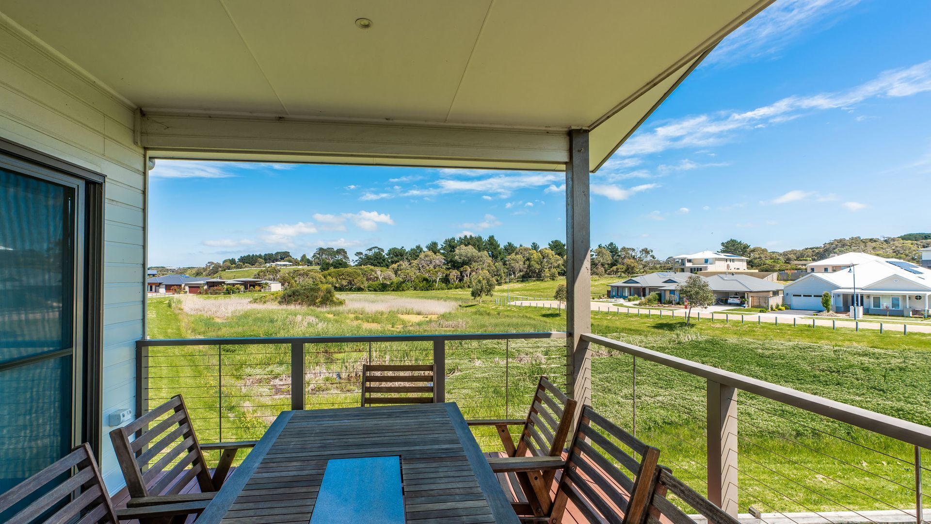 Un espacio al aire libre cubierto con una mesa y sillas, con vista a un campo cubierto de césped y edificios residenciales.